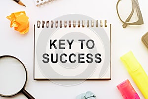 The text, the word Key To Success, is written in a notebook lying on white table with a pen, glasses and magnifier. Business