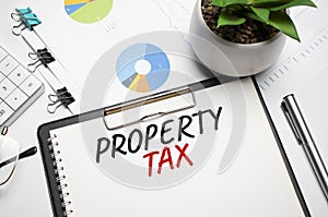 Text, the word Property Tax is written in a notebook lying on a black table with a pen, glasses and a calculator. Business concept