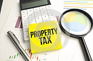 Text, the word Property Tax is written in a notebook lying on a black table with a pen, glasses and a calculator. Business concept