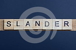 text the word slander from brown wooden small letters