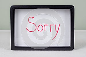Text word SORRY, black frame, on white table.