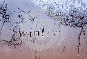 Text word winter scraped on frosty glass covered with white frost crystals on car blue window on winter cold clear morning
