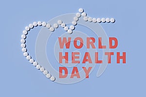 Text World Health Day. Group of white round pills forms heart figure next to heart rhythms from white pills on a blue