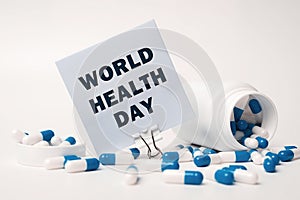 Text - World Health Day, written on sticky note near blue-white pills spilling out of pill bottle. Medical concept