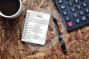 Text written on note pad with background of cup of coffee ,a pen and calculator. Reduce Expenses Concept