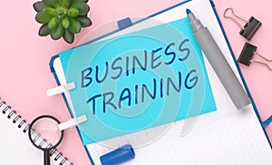 text 'BUSINESS TRAINING' on blue paper composition with stationery on color pink background. top view