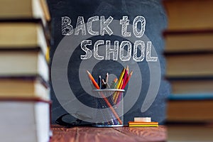 Textbooks and school supplies on a table, against a chalkboard background with chalk. Concept of school with copyspase