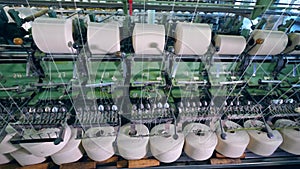 Textile factory machine coils bobbins with white fiber. Weaving machine working at textile fabric.