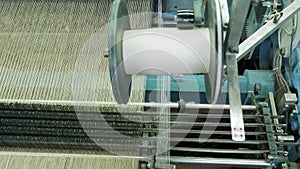 Textile factory production equipment in working process. close-up. big spool with white thread. Weaving mechanism