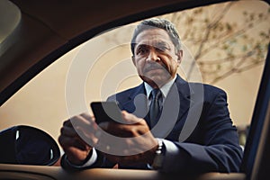 Texting and driving is serious business. Shot of a mature businessman using a phone while leaning against his car.