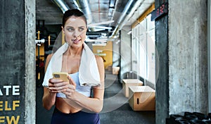 Texting sms. Young focused fitness woman in sportswear holding her smartphone and looking aside while exercising at gym