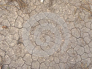 Texture of arid waterless cracked clay and some dry grass on the ground surface.