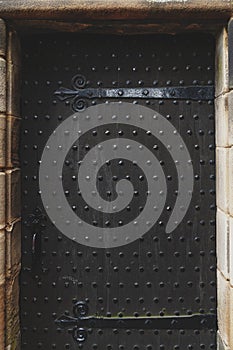 Texture background on ancient Scottish black wooden door decorated with metallic pins and bolt