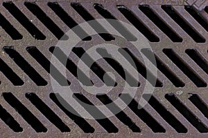 Texture background: city street brown old rusty metal iron gutter. Gray drain grate for waste and rain water.