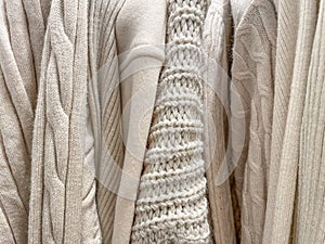 Texture background photo of different knitted sweaters and jumpers of beige cream color hanging in stack in the store.