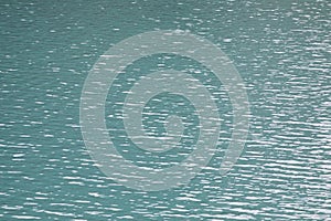 Texture background of turquoise water surface with ripples and light reflections