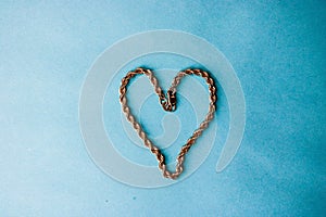 Texture of a beautiful golden dear festive chain of unique weaving in the shape of a heart on a blue background and copy space