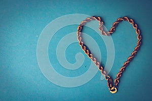 Texture of a beautiful golden dear festive chain of unique weaving in the shape of a heart on a blue background and copy space. C