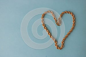 Texture of a beautiful golden dear festive chain of unique weaving in the shape of a heart on a blue background and copy space. C