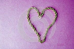 Texture of a beautiful golden festive chain unique weaving in the shape of a heart on a pink purple background and copy space