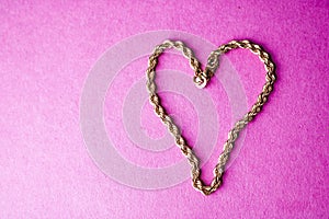 Texture of a beautiful golden festive chain unique weaving in the shape of a heart on a pink purple background and copy space