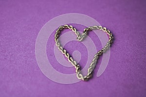 Texture of a beautiful golden festive chain unique weaving in the shape of a heart on a pink purple background and copy space