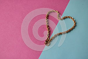 Texture of a beautiful golden festive chain unique weaving in the shape of a heart on a pink purple blue background and copy space