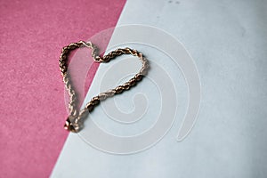 Texture of a beautiful golden festive chain unique weaving in the shape of a heart on a pink purple blue background and copy space