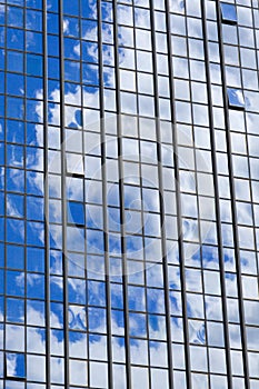 Texture of blue shiny glass skyscraper windows, buildings with reflection of white clouds and sky. The background