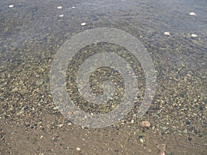 The texture of the bottom. Many small stones are visible under the clear water. Water ripples of the sea, sun rays on