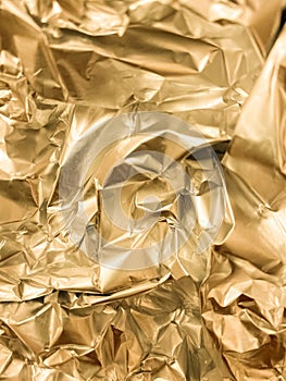 Texture of crumpled golden foil. Shiny festive background. Metallized paper.
