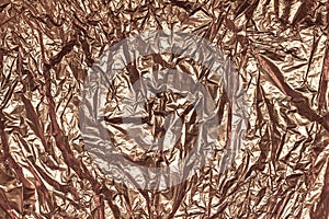 Texture of crumpled sheet of bronze foil, background closeup. Structure of creased shiny wrapping paper.