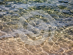 Texture of crystal clear light blue and turquoise transparent water with fine white sand base with bright reflection of sun in