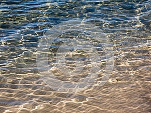 Texture of crystal clear light blue and turquoise transparent water with fine white sand base with bright reflection of sun in