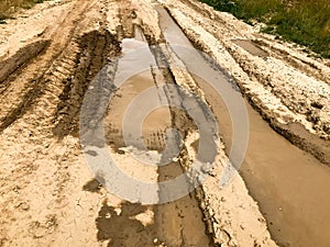 Texture of a dirty bad dirt road dirt road with puddles and clay drying mud with cracks and ruts. Off-road. The background