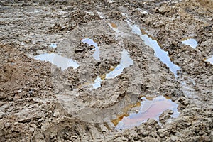 Texture of a dirty bad dirt road dirt road with puddles and clay drying mud with cracks and ruts. Off-road. The background