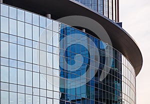 Texture of the facade of glass building of round shape with the reflection sky in it.