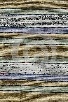 Texture of handmade carpet made on hand-loom, pattern of yellow, green, blue, white and black pastel vertical lines divided by thi