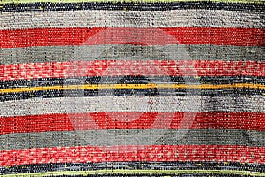 Textura ručně vyráběného koberce vyrobeného na ručním stavu, vzor různých červených, bílých, černých a žlutých svislých čar