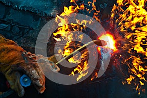 The texture of hot metal from acetylene welding. Welder's hands in protective gloves during operation.