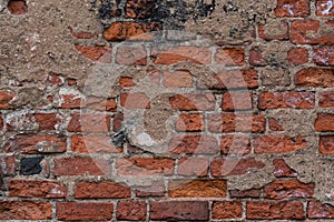 Texture of an old exterior uneven brickwork surface made of red bricks. Bricks are aged and weathered with mold, crumbled mortar