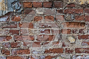 Texture of an old exterior wall surface made of red bricks. Bricks are aged and weathered with crumbled mortar and numerous cracks