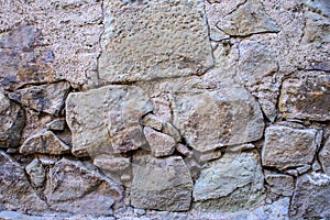 A texture of an old grey stone wall with concrete and big and small stones