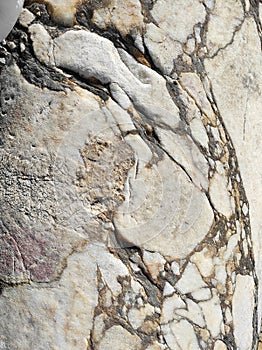 The texture of an old stone wall with pieces of white marble and gray pebbles, with cracks and veins