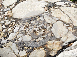 The texture of an old stone wall with pieces of white marble and gray pebbles, with cracks and veins