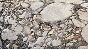 The texture of an old stone wall with pieces of white marble and gray pebbles, with cracks and veins