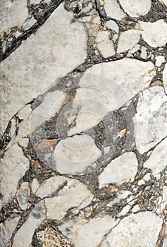 The texture of an old stone wall with pieces of white marble and gray pebbles, with cracks and veins