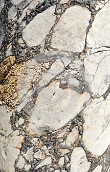 The texture of an old stone wall with pieces of white marble and gray pebbles, with cracks and veins