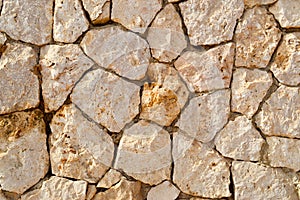 Texture of an old stone yellow wall from uneven different ancient friable stones of different shapes with sandy seams. The backgro