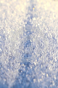 Texture and pattern of white ice and snow crystals close up in bright sunlight. Winter natural background